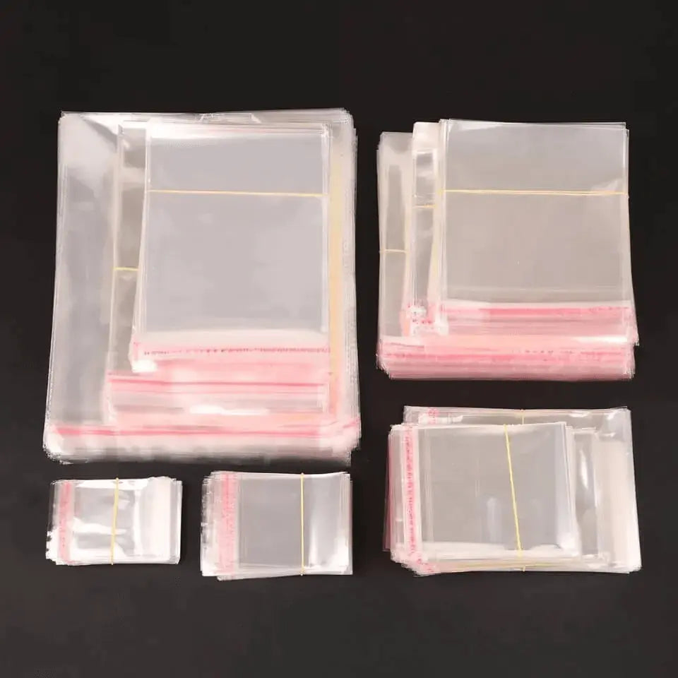 Transparante cellofaanzakjes met plakstrip in verschillende afmetingen, gebundeld op een zwarte achtergrond.