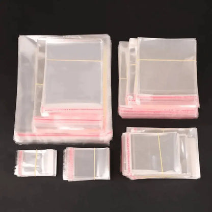 Transparante cellofaanzakjes met plakstrip in verschillende afmetingen, gebundeld op een zwarte achtergrond.